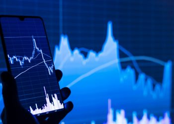 a person holding a cell phone in front of a stock chart
